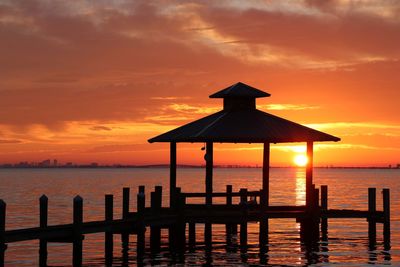 Silhouette gazebo by sea against sky during sunset