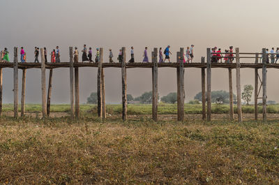 U bein teak bridge, myanmar - april 11, 2017: anonymous local people in casual clothes crossing taungthaman lake while walking on aged wooden teak bridge under sunset sky