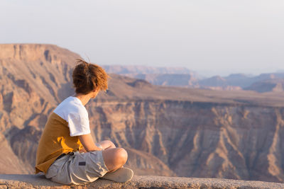 Woman sitting on mountain while looking at view