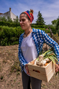 Smiling woman holding vegetables standing at farm