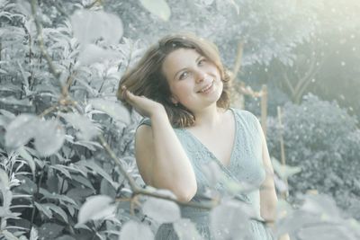 Portrait of smiling woman by plants during snowfall