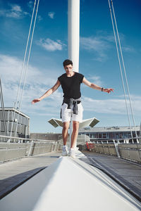 Full length of young man with arms outstretched against blue sky