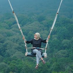 Full length of woman sitting on swing against forest