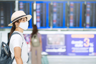 Woman wearing mask and hat looking away while standing at airport
