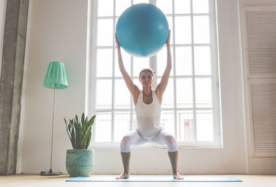 Full length of young woman exercising by window at home