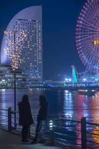 Rear view of people in illuminated city against sky at night