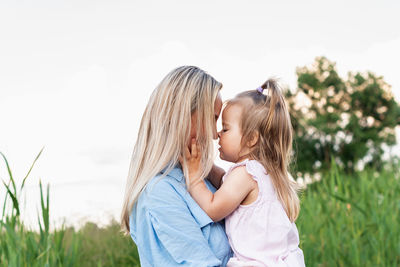 Rear view of woman embracing little girl, standing against sky