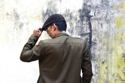 Rear view of mid adult man wearing cap standing against wall