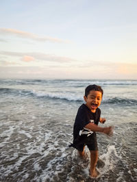 Full length of happy boy at beach against sky