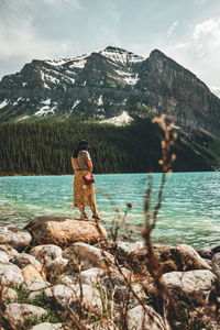 Woman standing on rock by lake against mountain
