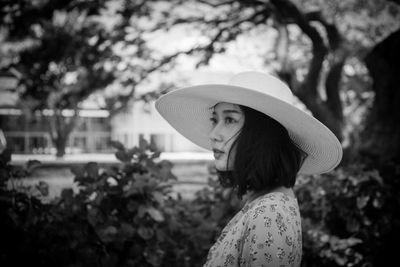 Portrait of woman with hat standing against trees