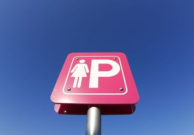 Low angle view of road sign against clear blue sky