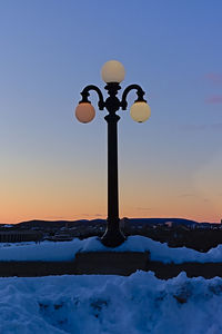 Street light on snow covered field against sky during sunset