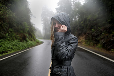 Portrait of smiling woman wearing raincoat while standing on road