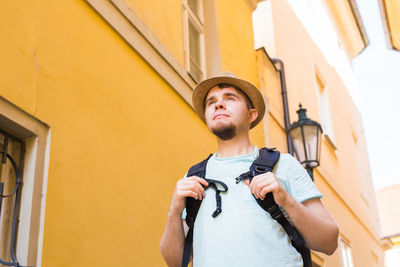 Young man looking away while standing against building