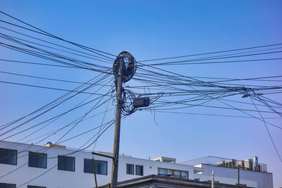 Low angle view of electricity pylon and buildings against clear blue sky