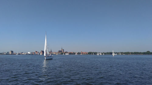 Sailboats sailing in river against clear sky