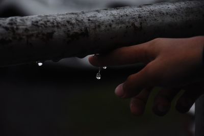 Close-up of hand touching raindrops on wood material