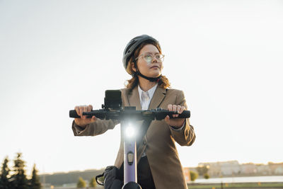 Thoughtful businesswoman riding electric push scooter