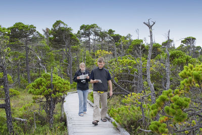 Full length of father and daughter walking on boardwalk amidst trees