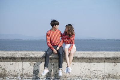Couple sitting together on retaining wall against sea