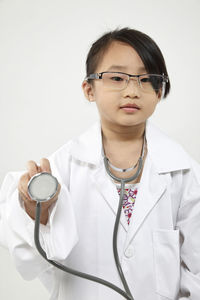 Portrait of cute girl in doctor costume holding stethoscope against white background