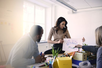 Male and female engineers discussing over diagram at table during meeting in office