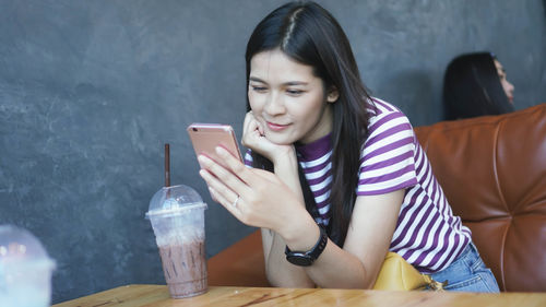 Young woman using mobile phone while sitting on table