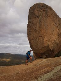 Rear view of man standing on rock against sky