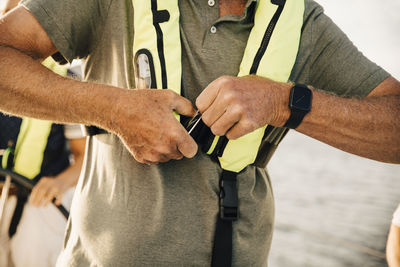 Midsection of senior man fastening belt of life jacket