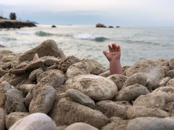 Person hand amidst pebbles at beach against sky