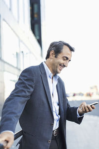 Happy businessman using mobile phone on sidewalk