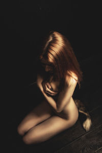 Naked woman sitting against black background