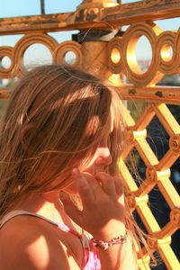 Side view of girl biting nails by fence