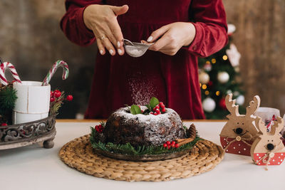 Midsection of woman dusting powder sugar on cake