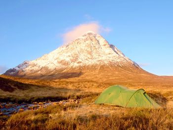 Green tent and snowy mountain peak. higland in scotland an marvelous sunny winter day. hikers tent