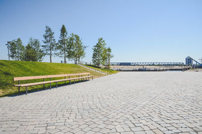 Empty footpath by street against clear blue sky