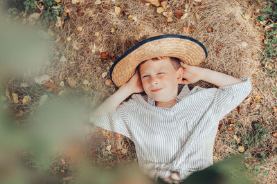 Little preschooler farmer in straw hat and rustic  shirt lies on the straw and yellow autumn leaves