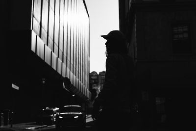 Side view of silhouette man standing on street against buildings at night