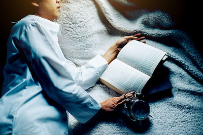 Woman with alarm clock and book sleeping on bed