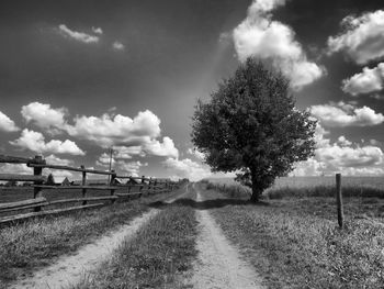 Road passing through field against cloudy sky