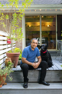 Smiling hispanic male sit on his deck with black dog