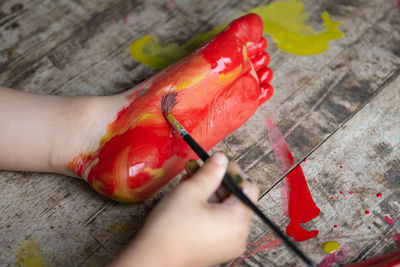 Cropped hand of boy painting barefoot at home