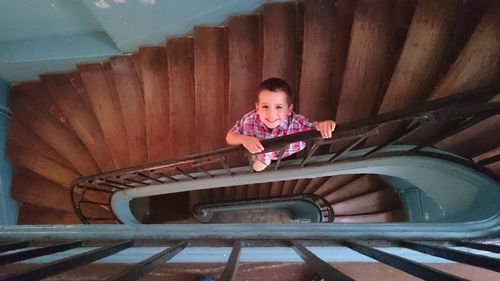 High angle portrait of boy smiling while standing on spiral staircase