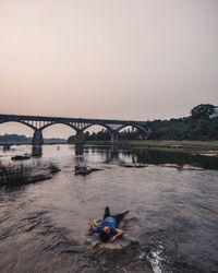 Man on bridge over river against sky during sunset