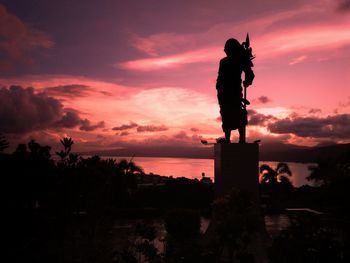 Silhouette of statue against cloudy sky during sunset