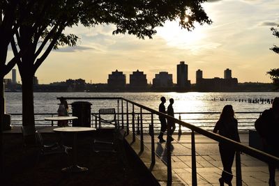 People on walkway against hudson river during sunset in city