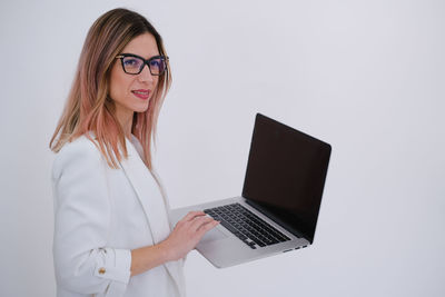 Portrait of young woman using laptop while standing against white background
