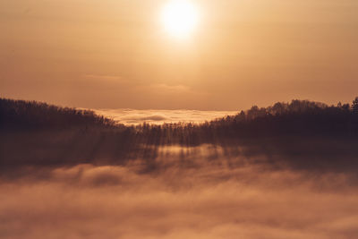 Sunset over a sea of clouds with a view of the sun passing through the forest on the other hill