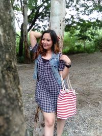 Smiling woman standing against tree trunk